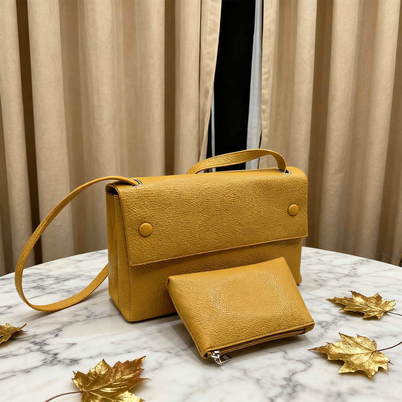 Yellow handbag and wallet set on a marble surface with gold leaves and curtains in the background